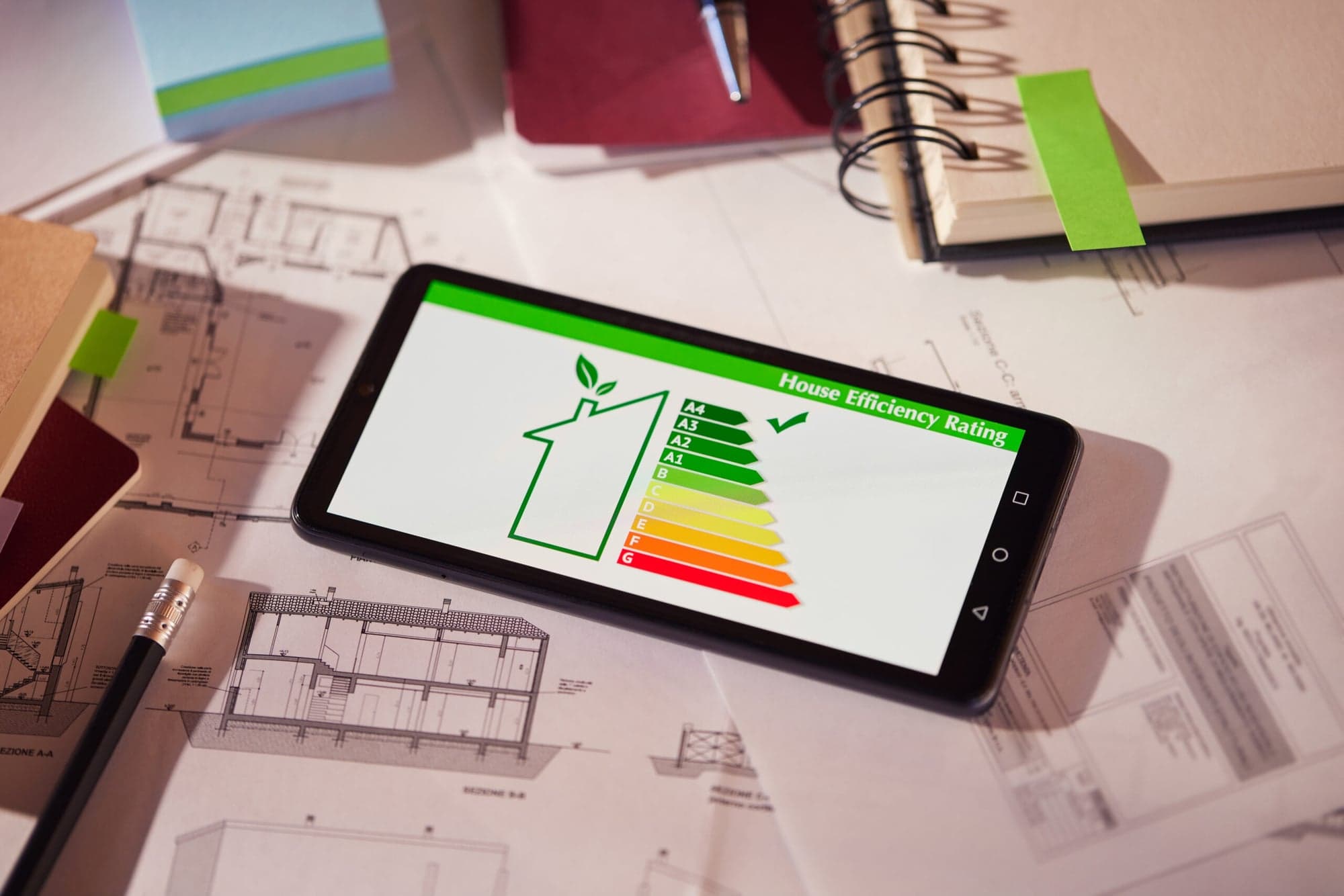 Energieausweis und Effizienzklassen auf Smartphone neben Bauplänen – Energieberatung für Gebäude Wiesbaden